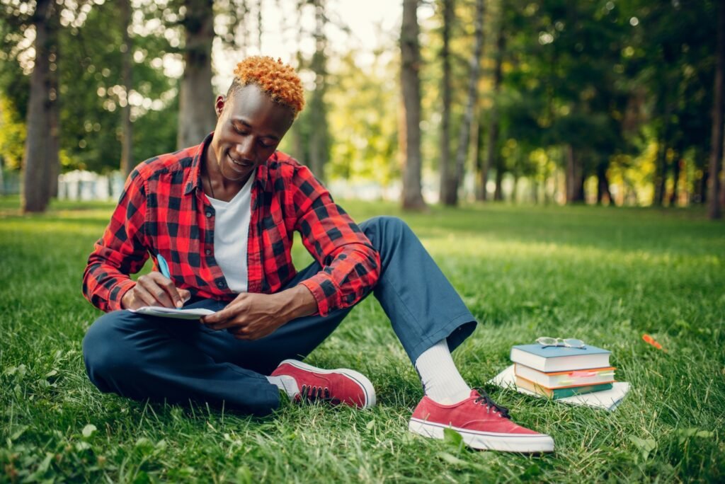 Black student writing in notebook on the grass