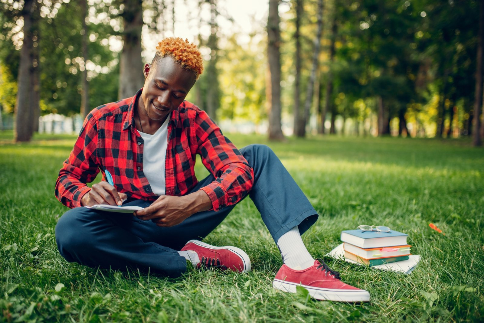 Black student writing in notebook on the grass