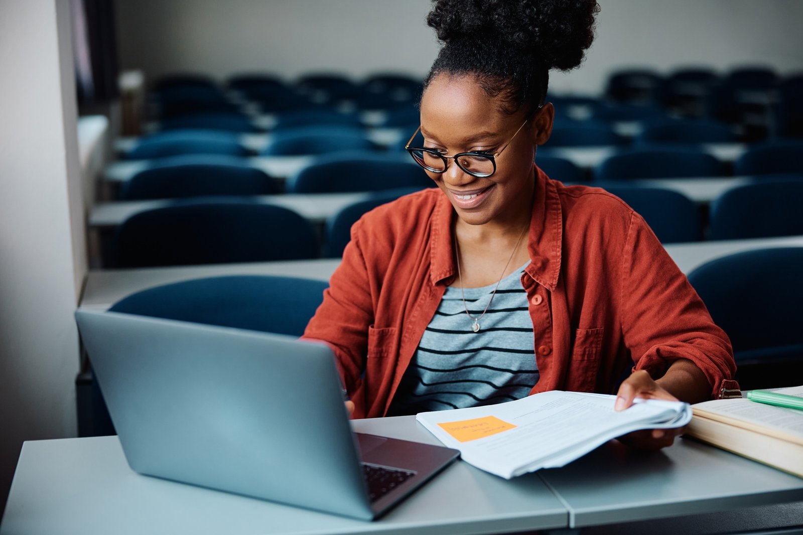 Happy black female student e-learning on laptop at university classroom.