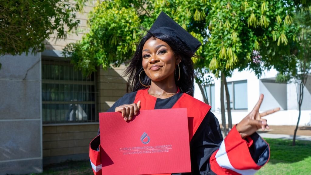 Nigerian university graduate in cap and gown holding a certificate folder