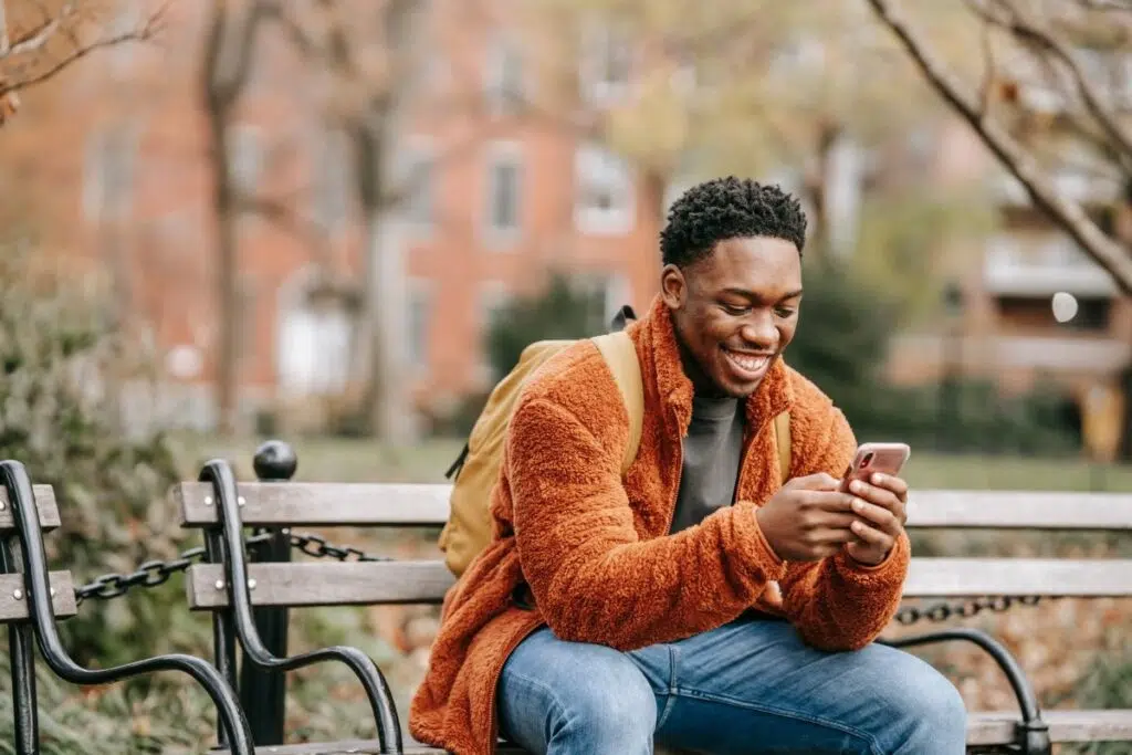 Young Nigerian man sitting outside smiling at his phone while recovering his JAMB profile by SMS