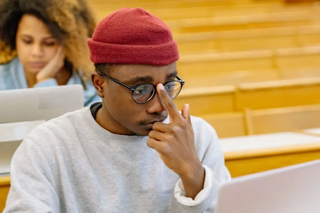 Nigerian student in a lecture hall pausing at his laptop while checking why his JAMB admission letter will not print