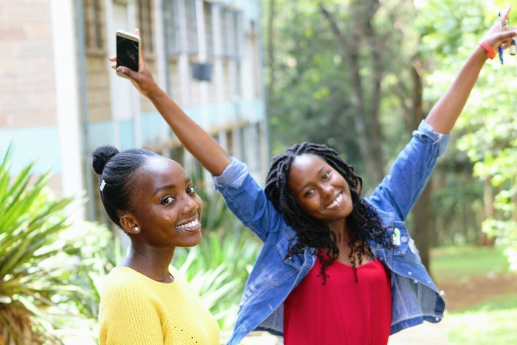 Two young Nigerian students on a university campus, one holding up her phone