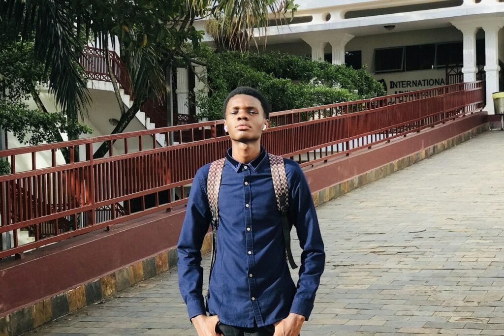 A young Nigerian fresher with a backpack standing on a university walkway on his first day on campus, ready for fresher clearance