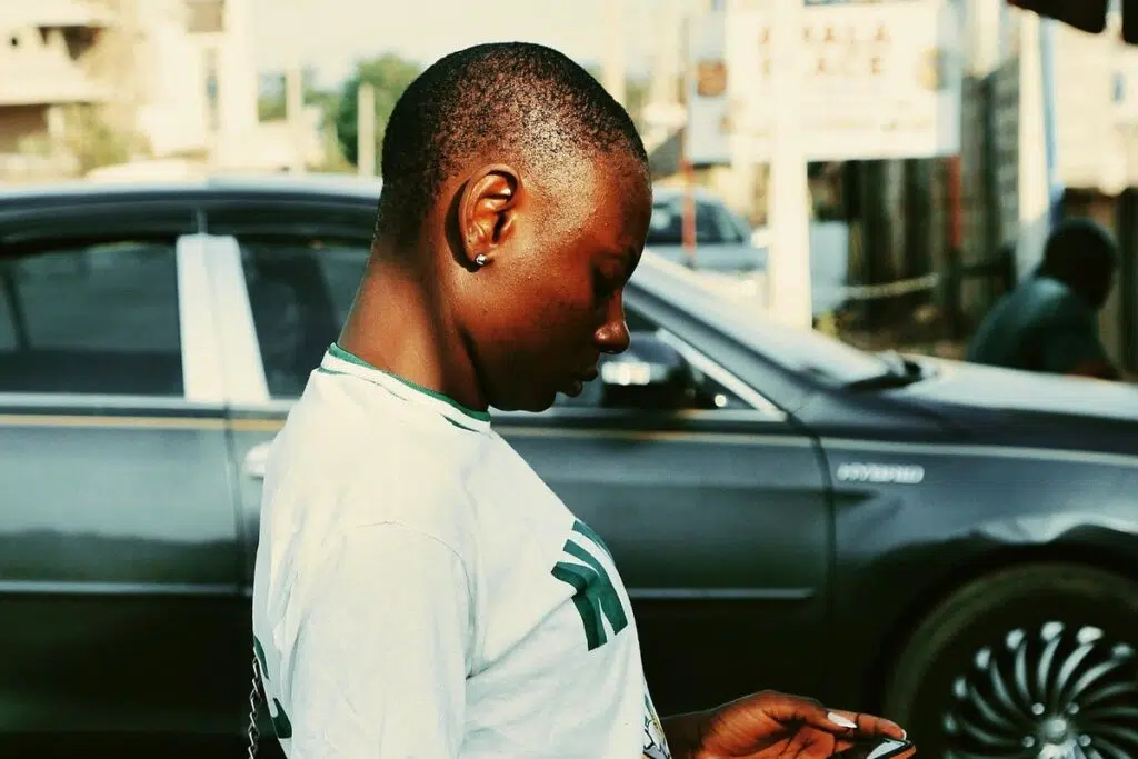 Young Nigerian woman checking her phone on a street, waiting on the NECO result 2026