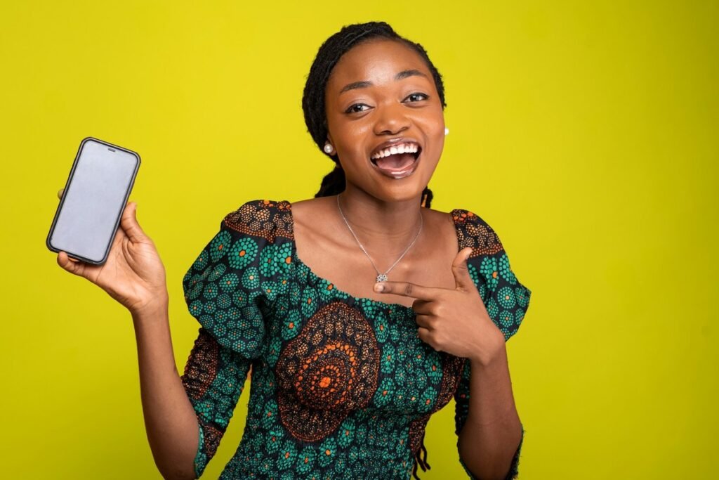 Young Nigerian woman in an ankara dress smiling and holding up her phone after checking her NECO result