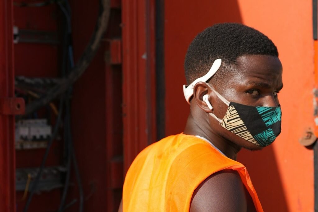 Young Nigerian electrical engineering student in an orange safety vest beside an open electrical panel during SIWES